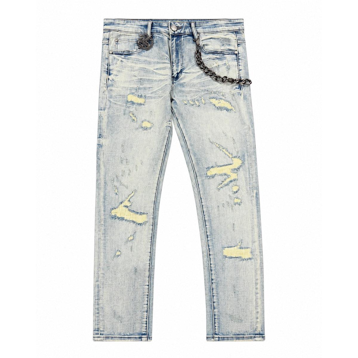 Light wash skinny jeans with heavy distressing, yellow underlay patches, and a detachable metal chain accessory.