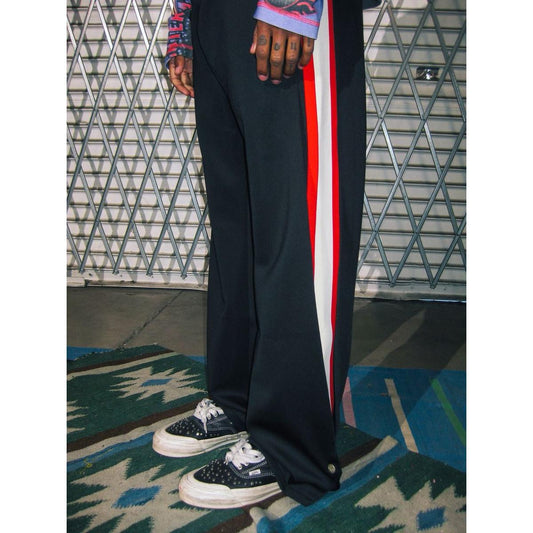 Black wide-leg sweatpants with red and white racing stripes and snap-button hem details in a relaxed streetwear fit.