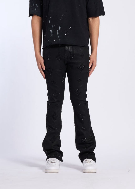 A model wearing Crysp Denim | Onyx Rhinestone Stacked Pants - Black Wax styled with a black shirt and sneakers.