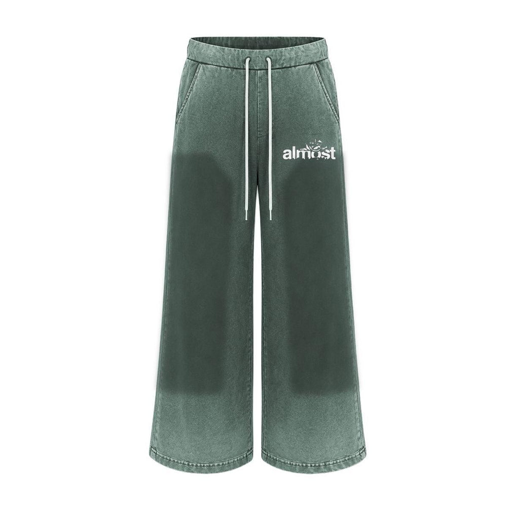 Green flared sweatpants with a vintage wash, white drawstring waist, and Almost Someday graphic logo on the hip.