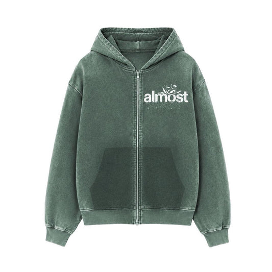 Almost Someday green zip-up hoodie with white graphic logo, front pockets, and ribbed hem in a streetwear style.