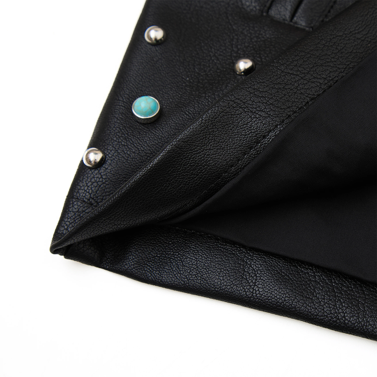 Close-up of a black leather jacket with silver studs and a turquoise stone on a white background