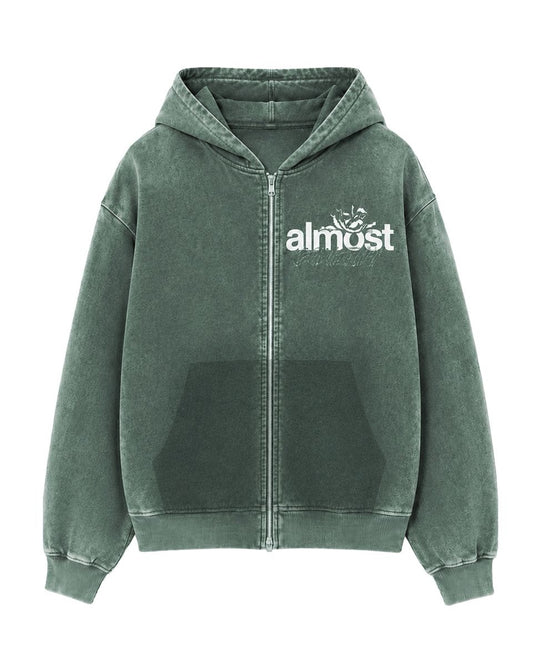 Almost Someday green zip-up hoodie with white graphic logo, front pockets, and ribbed hem in a streetwear style.